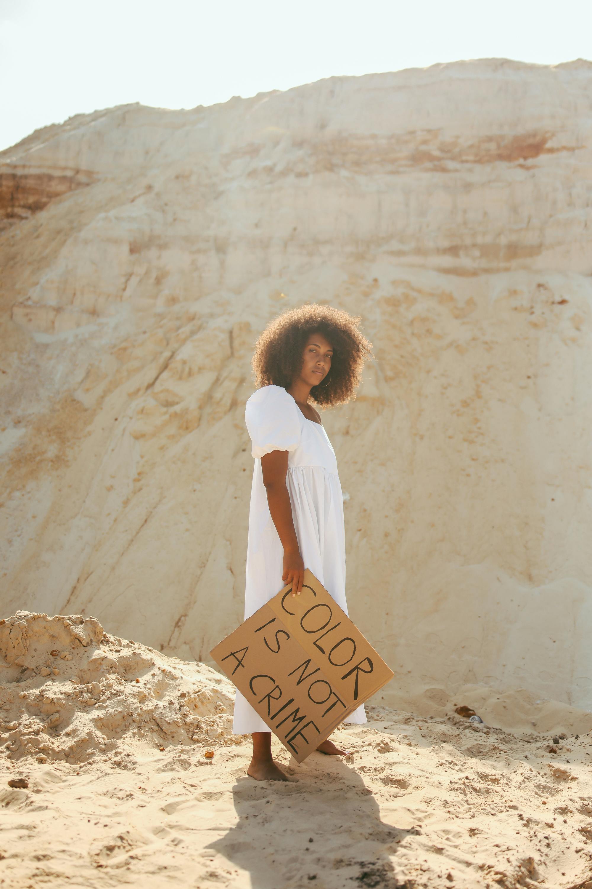 woman in white dress standing on a sand holding a placard