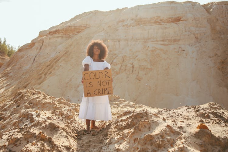 Woman Standing In The Desert And Holding A Cardboard Sign With A Slogan 