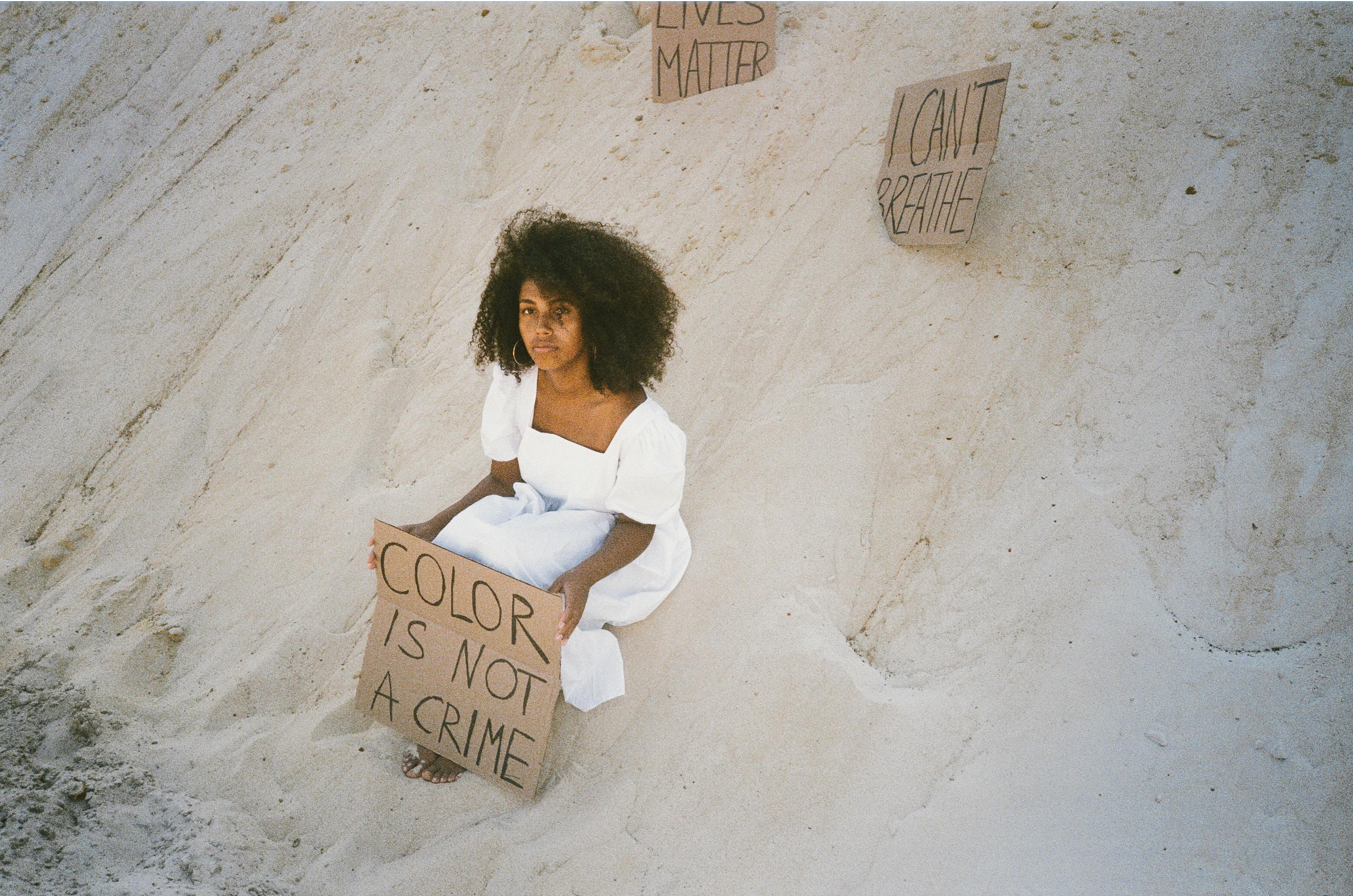 Woman with afro hair sits on sand dune, holding a protest sign. Inspirational image.
