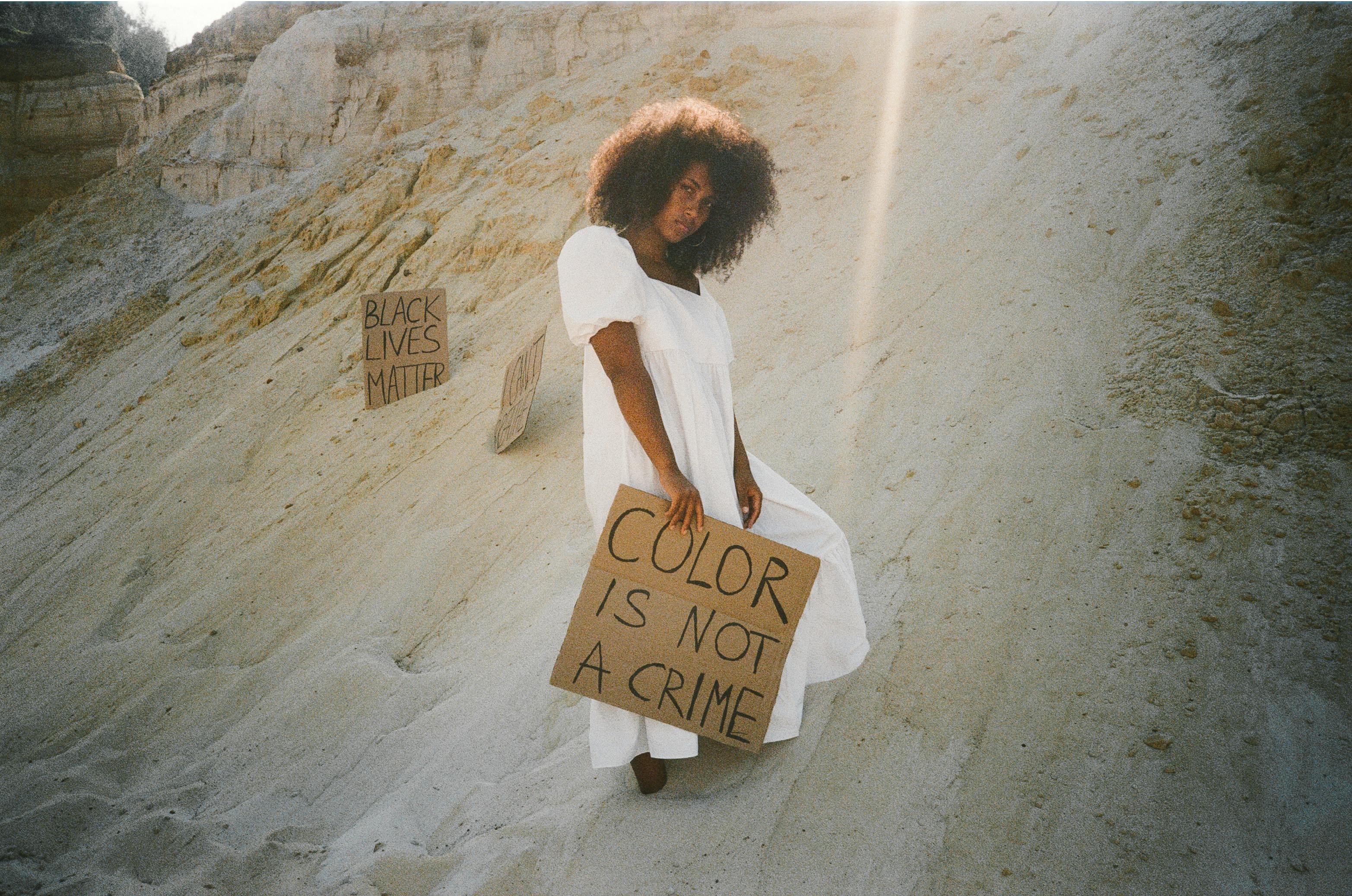 一名妇女站在沙漠中，举着“肤色不是犯罪”和“黑人的命也是命”的标语，倡导激进主义