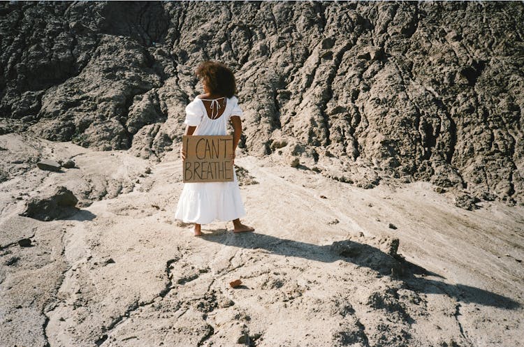 Woman Standing In The Desert And Holding A Cardboard Sign With A Slogan 