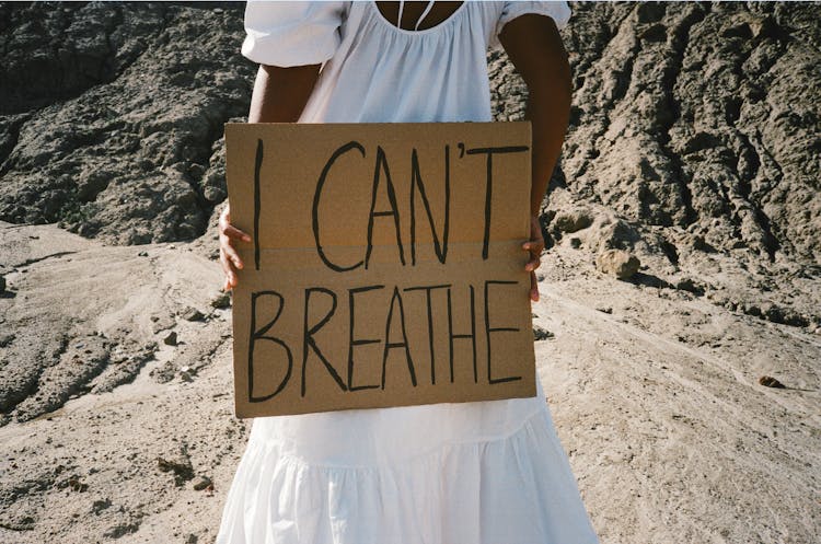 Woman Standing In The Desert And Holding A Cardboard Sign With A Slogan 