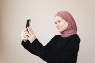 一名年轻穆斯林妇女戴着头巾，在室内用智能手机自拍