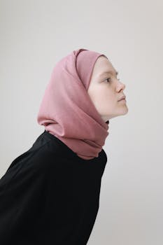 Profile portrait of a young Muslim woman wearing a pink hijab against a neutral background.