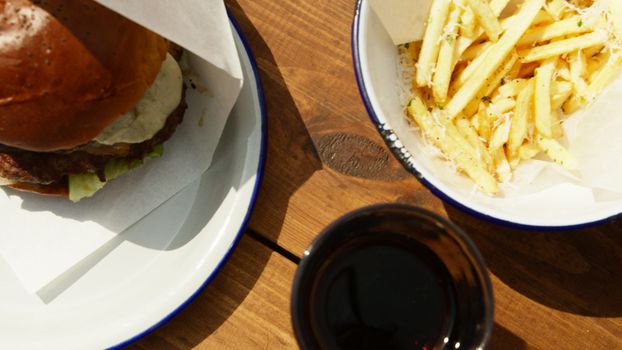 Close-up of a delicious hamburger and fries served on ceramic plates outdoors.