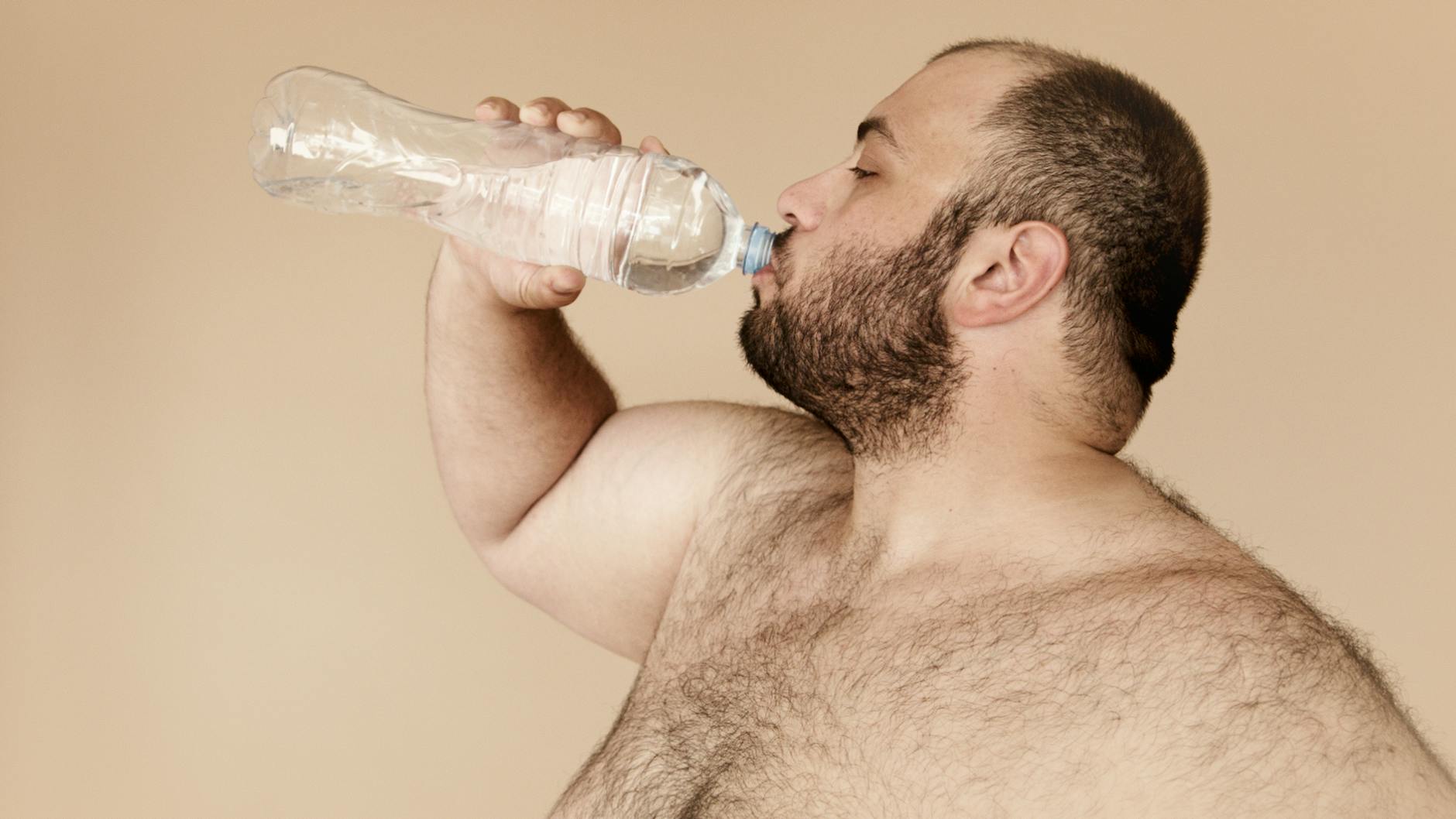 Bearded man drinking water from plastic bottle to stay hydrated and healthy.