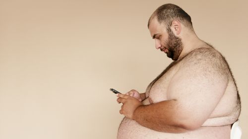 Free Side view of an overweight man using a smartphone indoors, showcasing modern technology usage. Stock Photo