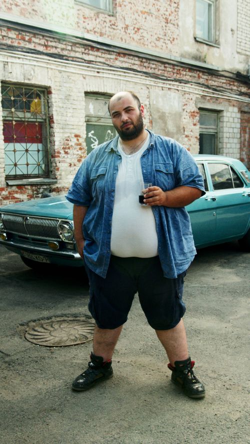 Free A relaxed man in casual attire stands in front of a vintage car in an urban alley. Stock Photo