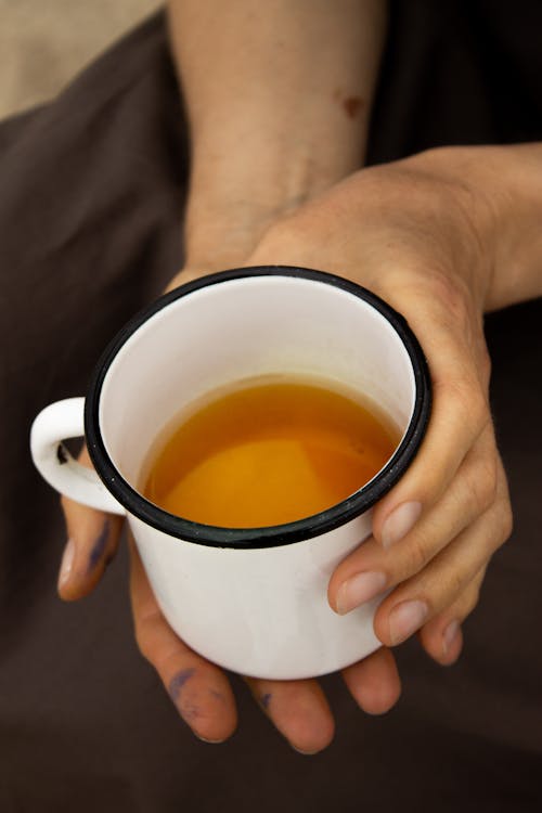 Free High angle crop anonymous female with aromatic fresh tea poured in white metal cup Stock Photo