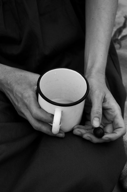 Black and white high angle of crop anonymous female resting in nature with cup of hot drink and cherry