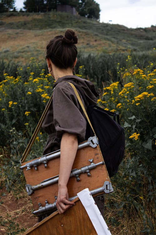 Side view of unrecognizable female artist with equipment for painting of rural environment