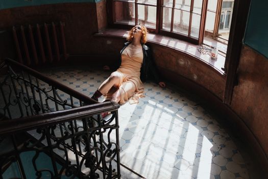 Woman in leather jacket sitting on vintage tiled floor by a large window.