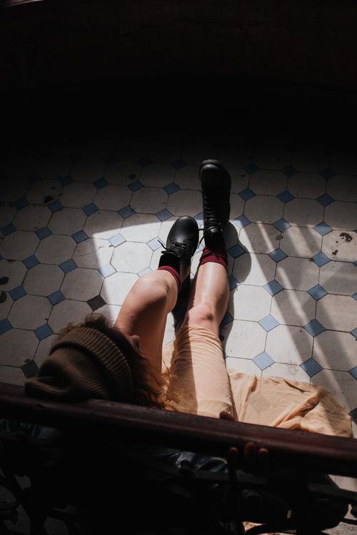 Free A woman in boots sits on a vintage tiled floor, bathed in moody lighting, creating a dramatic fashion image. Stock Photo