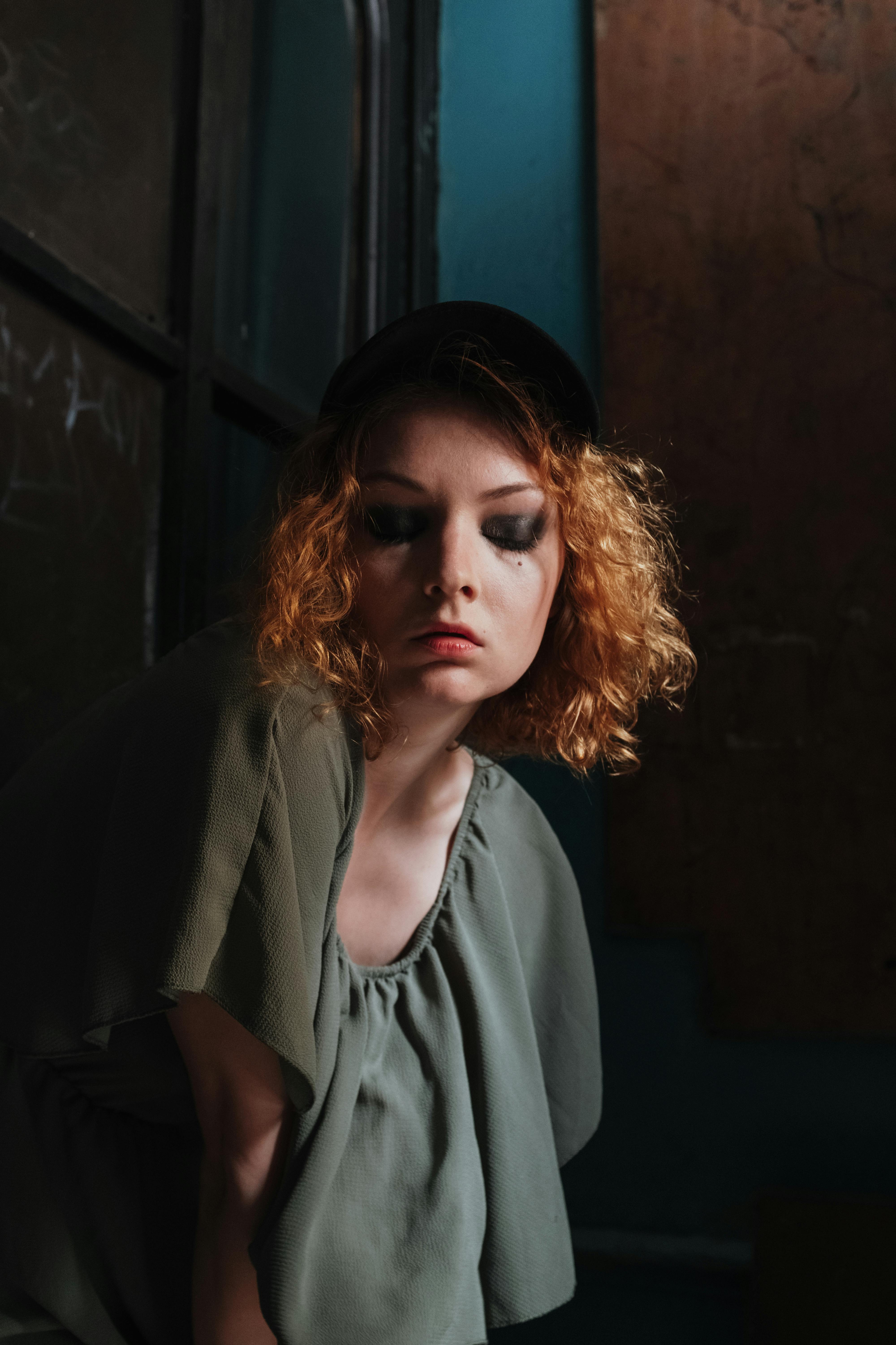Artistic portrait of a redhead woman with smoky eyes in a vintage indoor setting.