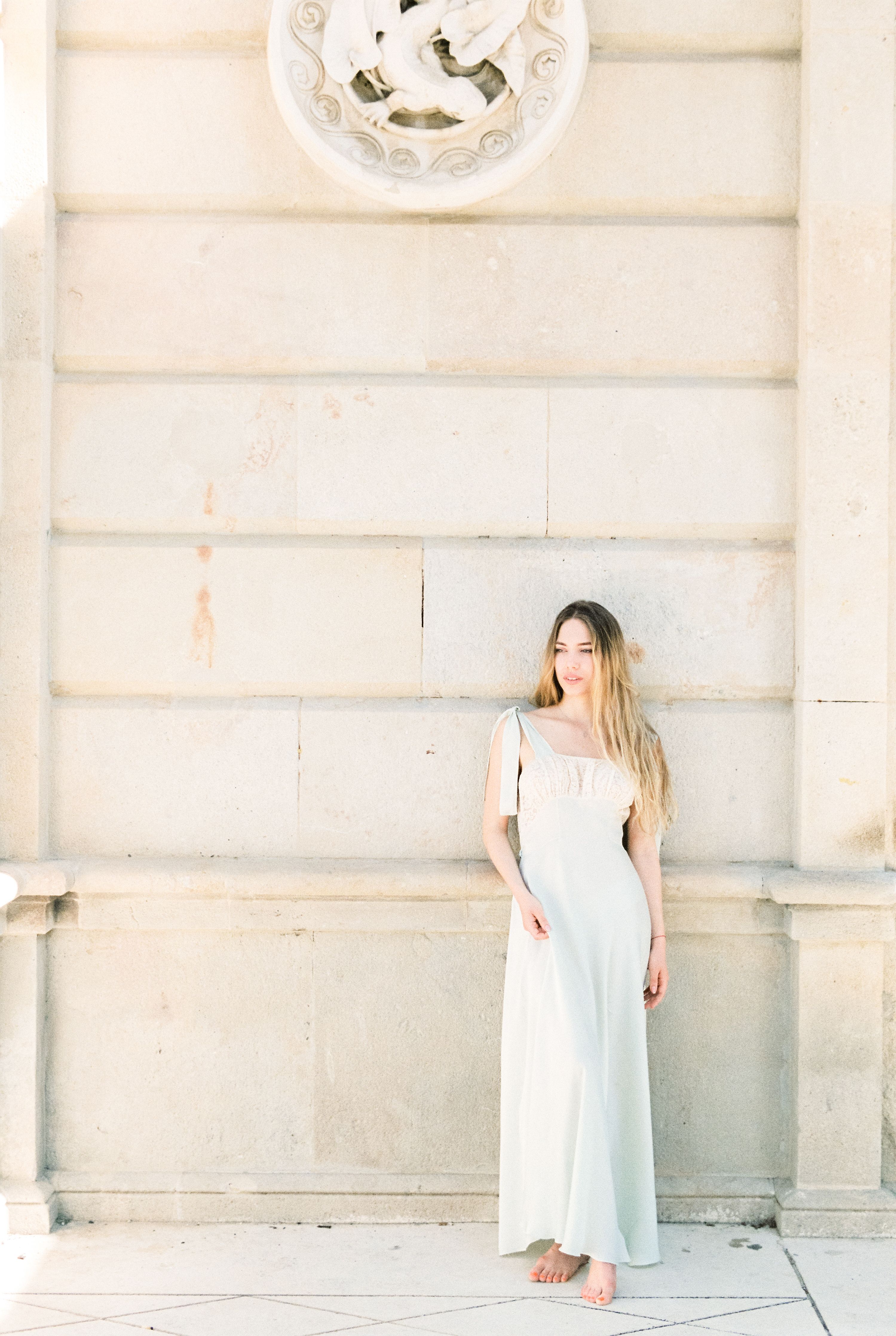 A Woman in White Dress Standing Beside a Concrete Wall · Free Stock Photo