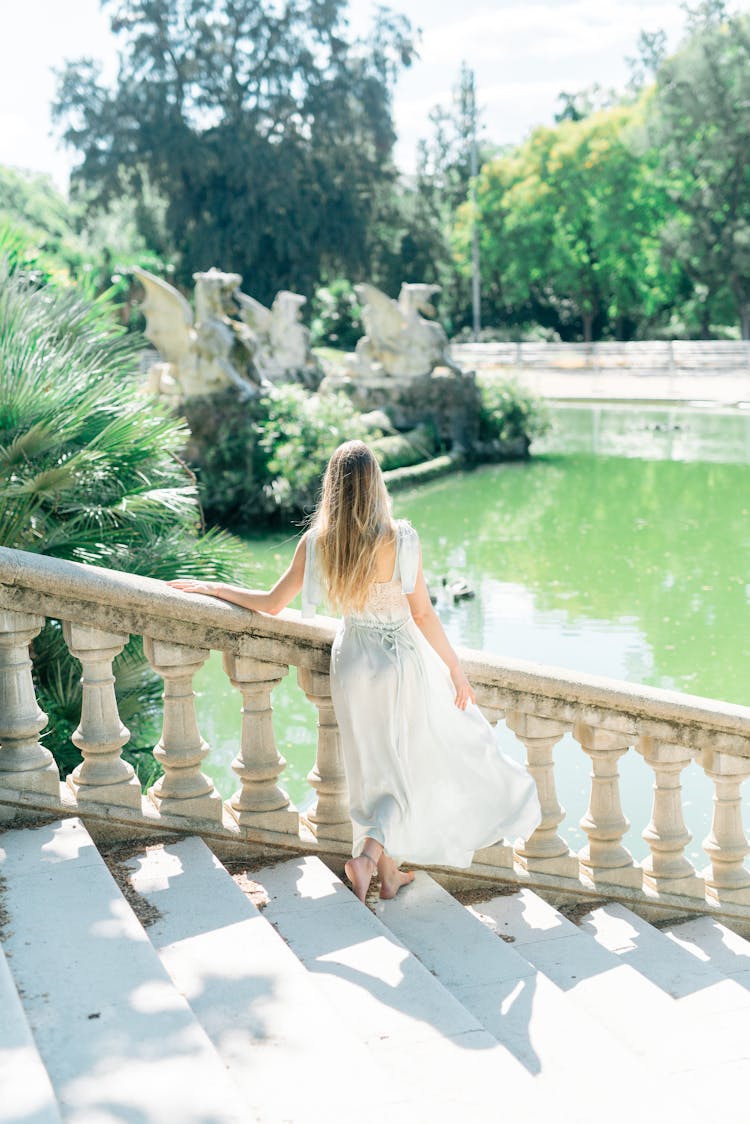 A Woman In White Dress Standing On The Steps Beside The Banister