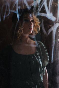 透过涂鸦覆盖的窗户，反射出一位卷发女子的喜怒无常肖像