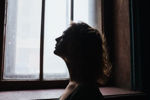一位卷发女子的剪影望向窗外，为室内营造出戏剧性而沉思的氛围
