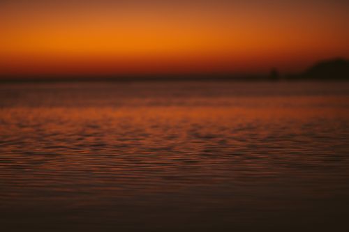 Free A calming view of the ocean surface at sunset with warm, vibrant hues in the sky. Stock Photo