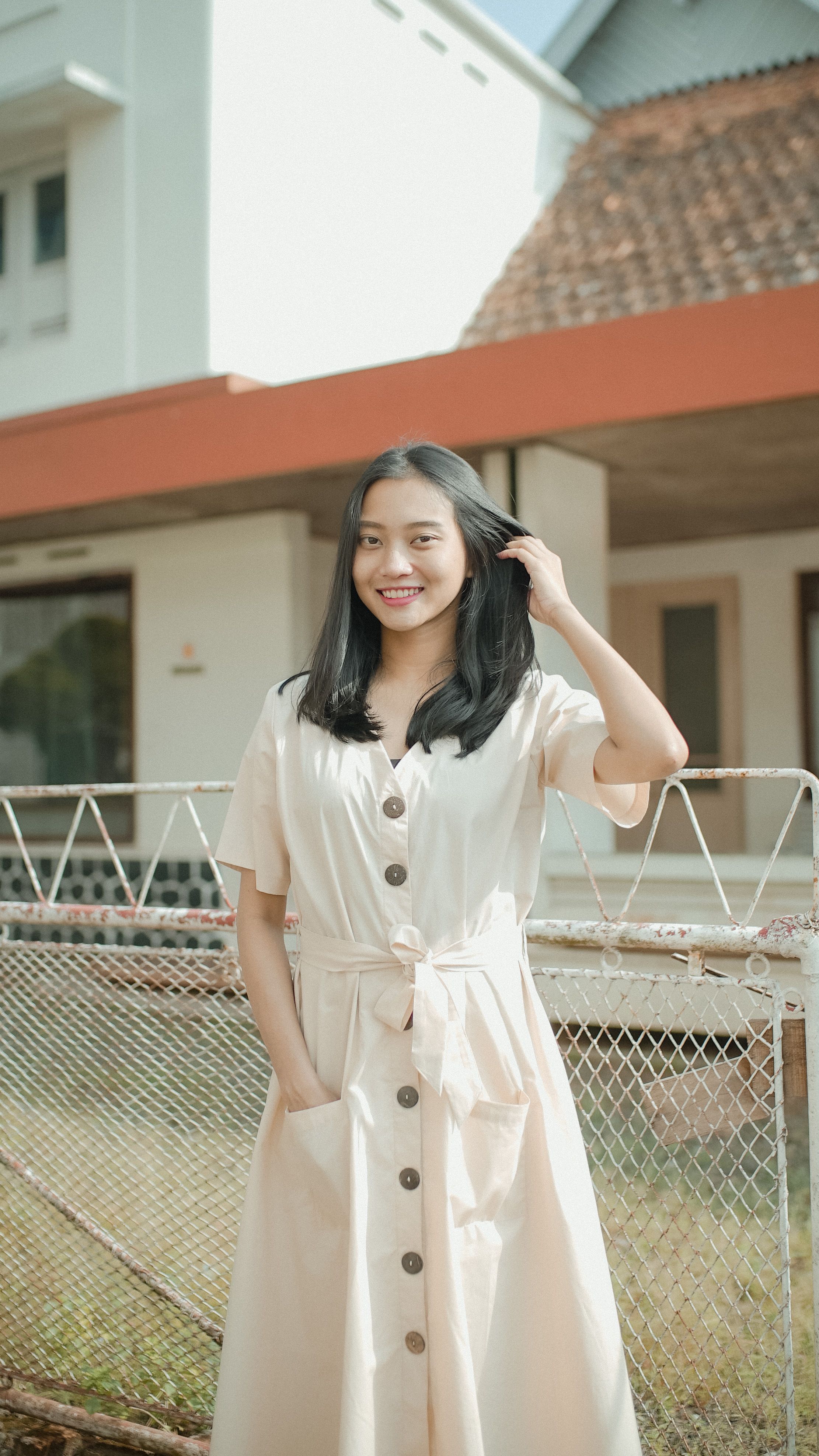 A young woman smiles while standing outside wearing a casual summer dress, exuding joy and style.