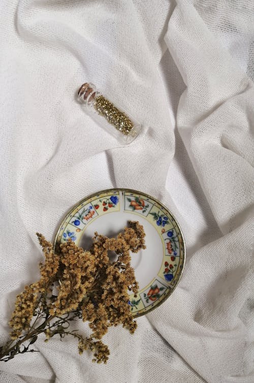 Composition of dried flowers on ceramic plate above white cloth