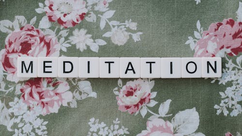 Free A Word Meditation Spelled with White Letter Blocks on a Floral Textile
 Stock Photo