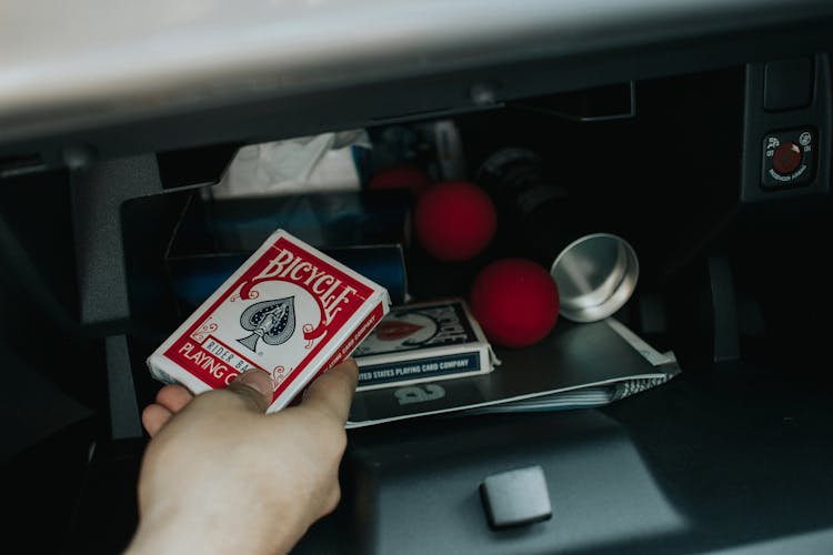 A Person Holding A Pack Of Bicycle Playing Cards From A Glove Compartment