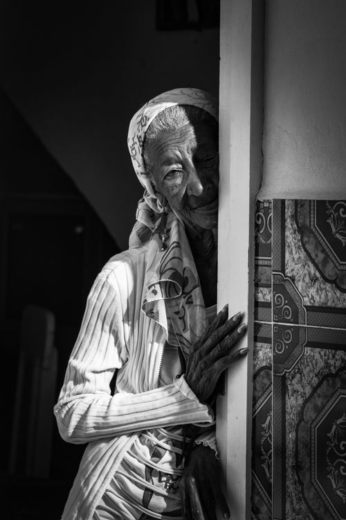 Free Black and white of crop elderly female in headscarf looking at camera while standing with shadow on face near wall Stock Photo
