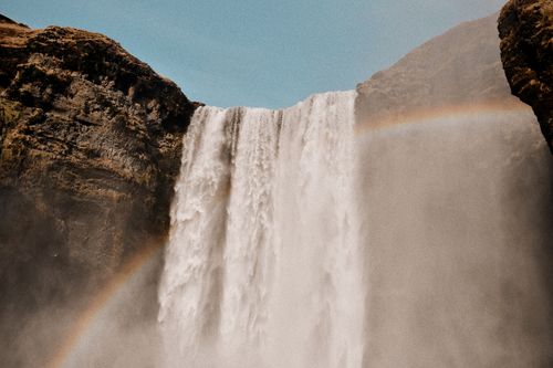 Free A stunning waterfall cascades with a vibrant rainbow arching across misty air, captured outdoors. Stock Photo