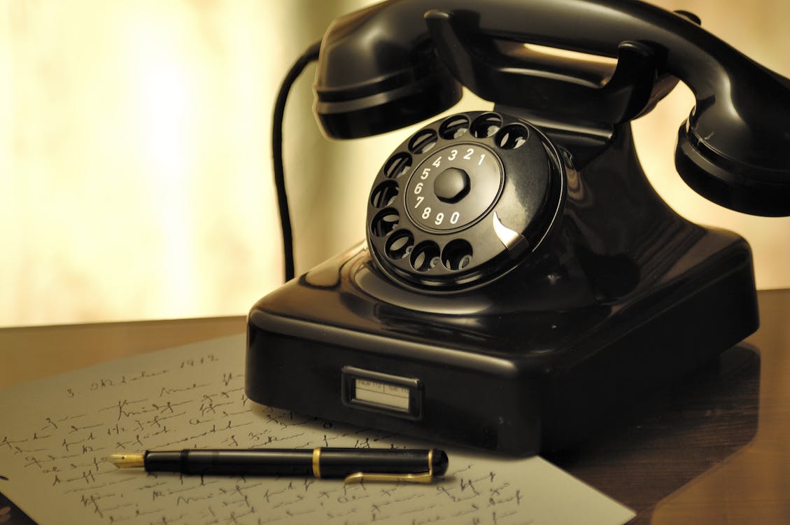 Black Rotary Telephone Beside Ball Pen on White Printed Paper