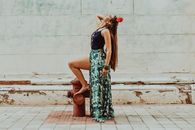 Side view of young content barefoot female in ornamental clothes and floral adornment on head looking up while touching hair on street