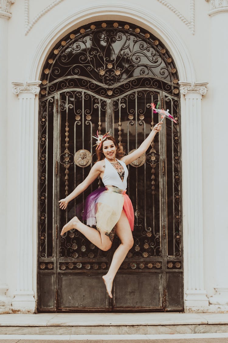 Stylish Woman In Modern Apparel Jumping Near Old Building Door