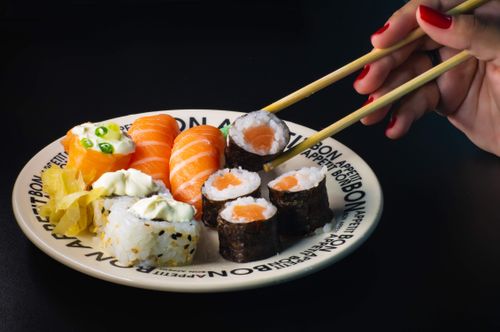Free A vibrant sushi platter with hand using chopsticks, featuring salmon, maki rolls, and garnishes. Stock Photo