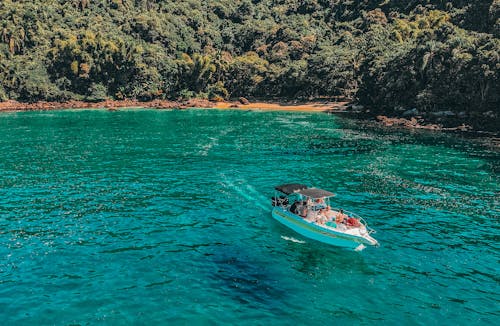 Scenery of modern white boat with travelers floating on crystal clear turquoise seawater near coast covered with lush tropical vegetation