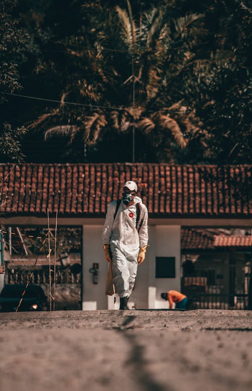Free Full body anonymous person in protective hazardous materials suit and respirator walking in rural area in tropical country during coronavirus epidemic Stock Photo