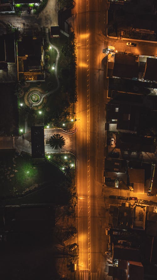 Aerial top view of modern suburban houses and empty asphalt road illuminated by electric lights at summer night