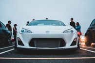 Modern white bodywork of parked car in front of group of drivers in twilight