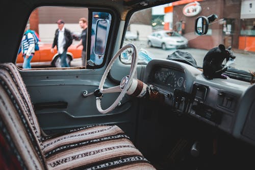Vintage cabin of retro car with dashboard behind steering wheel and car seat on modern city