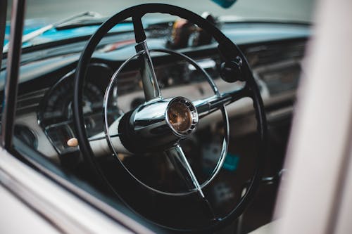 Closeup of stylish interior of vintage car with black metal steering wheel and dashboard