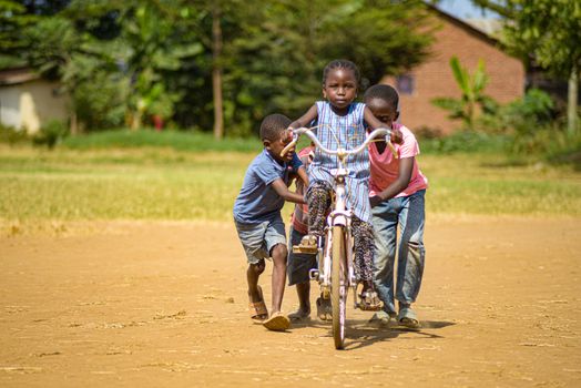 Three children playfully push a bicycle on a sunny day in Morogoro, Tanzania.