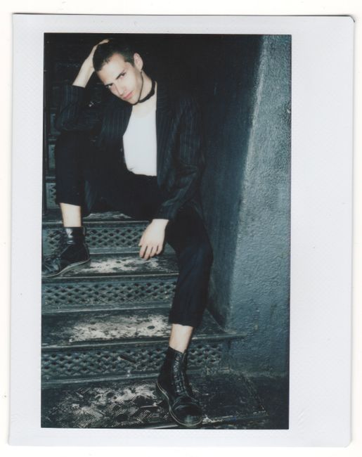 Vintage-style Polaroid of a stylish man sitting on stairs in dim light, exuding a retro and edgy vibe.