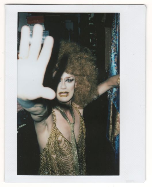 A vibrant drag performer poses dramatically in a lively nightclub atmosphere.