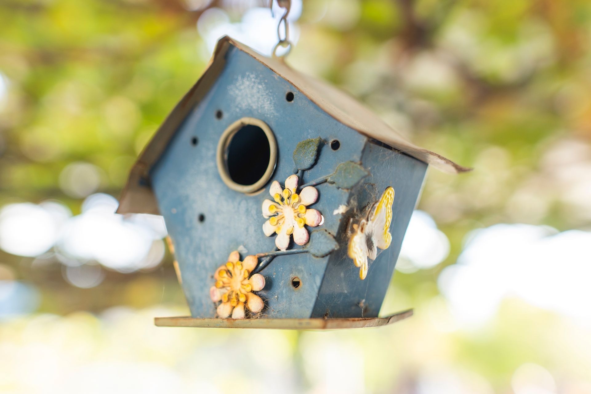 Close-up of a decorative blue birdhouse with floral designs, hanging outdoors in a garden in Bodrum, Türkiye.