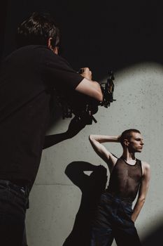 A photographer captures a model in dramatic outdoor lighting against a concrete wall.