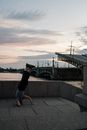 日落时分，一名男子在城市堤岸上倒立，身后是桥梁和城市天际线