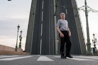 Man in White Crew Neck T-shirt and Black Pants Standing Near Gray Building