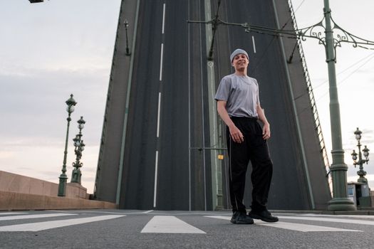 Man in White Crew Neck T-shirt and Black Pants Standing Near Gray Building