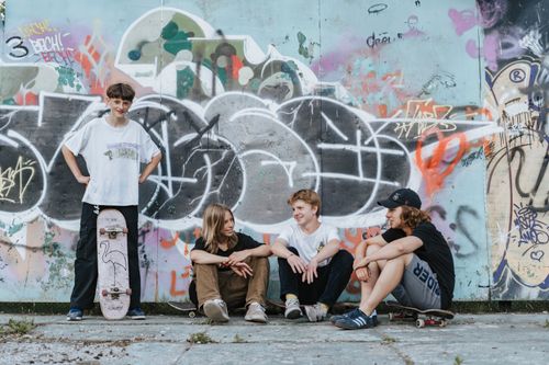 Free Four teenagers enjoying a casual skateboarding hangout in front of a vibrant graffiti-covered wall. Stock Photo