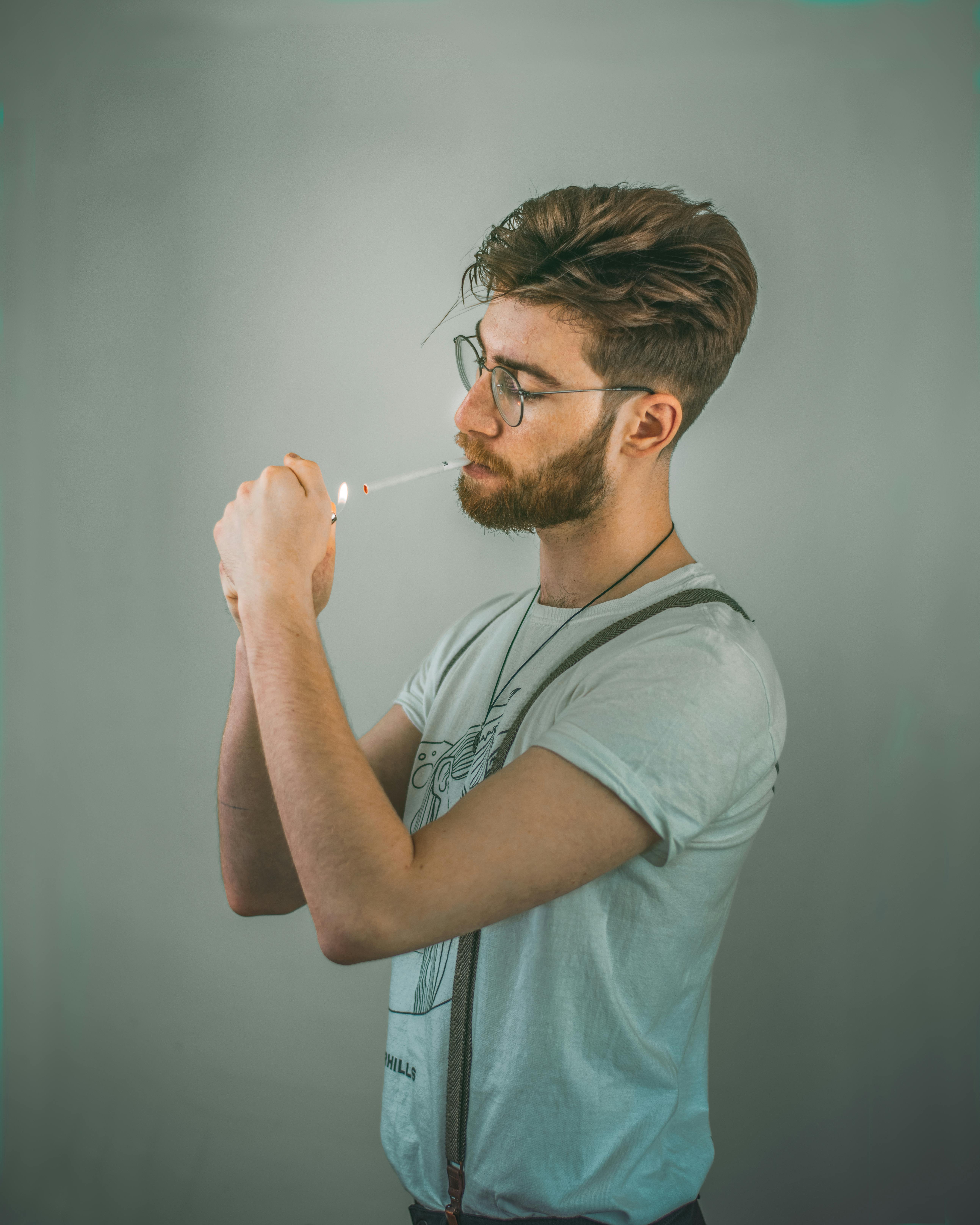 bearded man in light green shirt lighting a cigarette