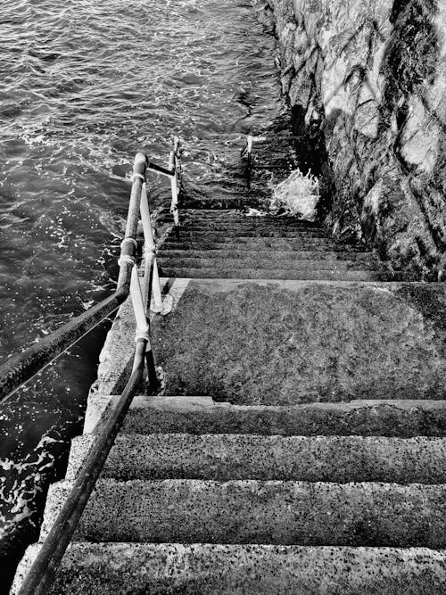 Black and white photo of old empty stairway with  railing leading to water